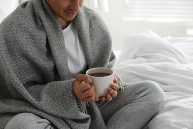 Photo of Man covered with warm grey plaid enjoying hot morning drink in bedroom, closeup