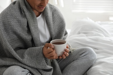 Man covered with warm grey plaid enjoying hot morning drink in bedroom, closeup