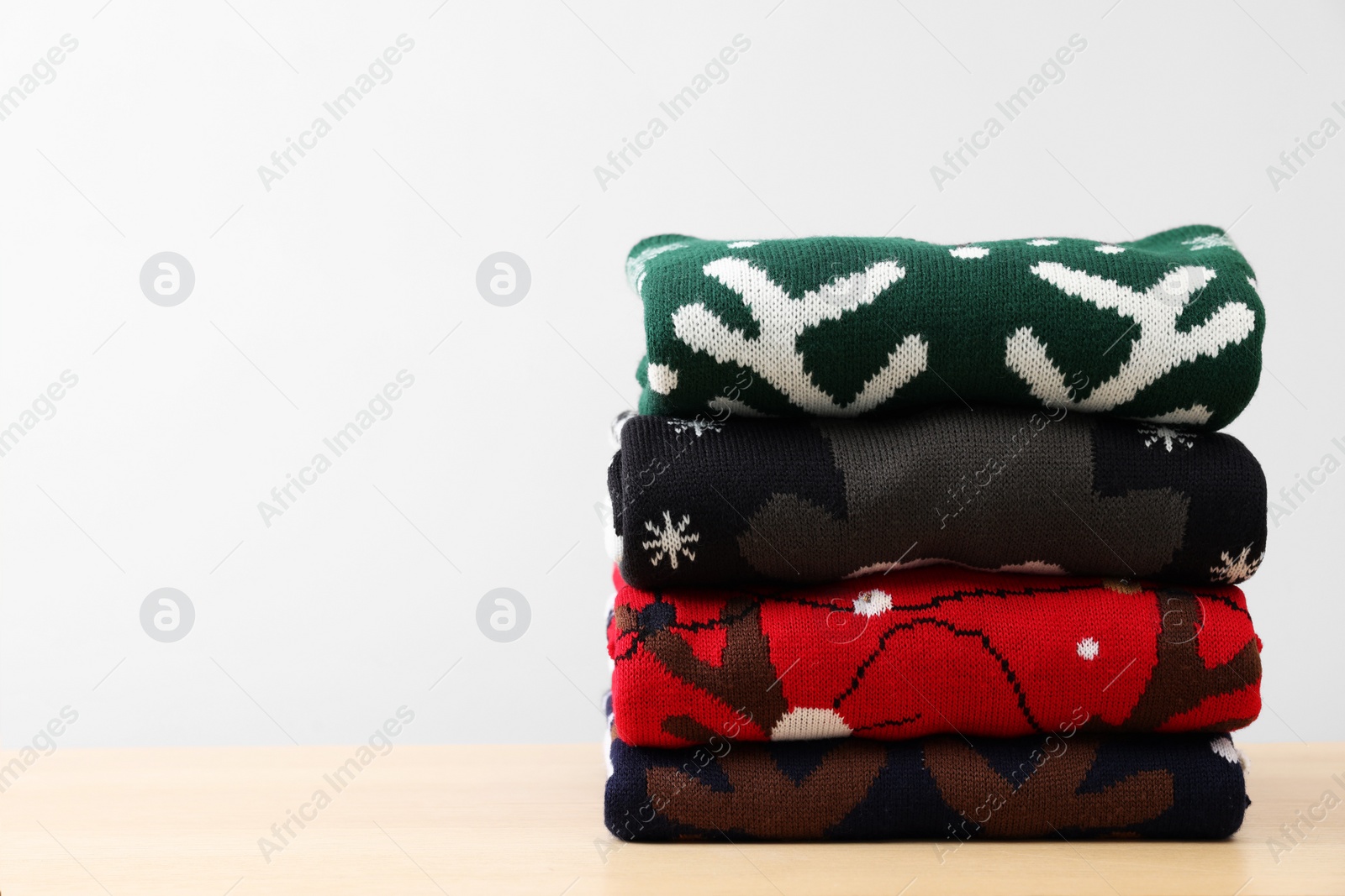 Photo of Stack of different Christmas sweaters on table against light background. Space for text