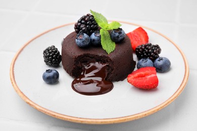 Plate with delicious chocolate fondant, berries and mint on white tiled table, closeup