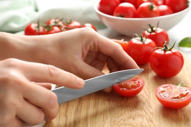 Photo of Woman cutting fresh cherry tomatoes on board at table, closeup