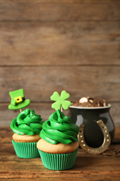 Decorated cupcakes and pot with gold coins on wooden table. St. Patrick's Day celebration