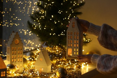 Photo of Woman holding decorative house near Christmas decorations on window sill indoors, closeup