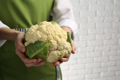 Photo of Woman holding fresh cauliflower against white brick wall, closeup. Space for text
