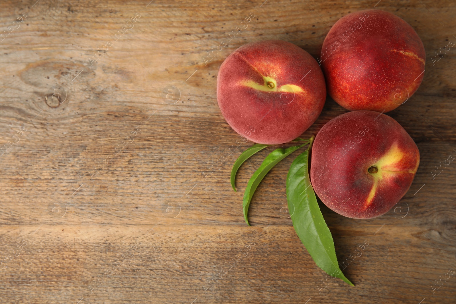 Photo of Fresh peaches and leaves on wooden table, top view with space for text