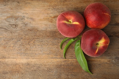 Photo of Fresh peaches and leaves on wooden table, top view with space for text