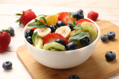 Photo of Tasty fruit salad in bowl and ingredients on wooden table, closeup