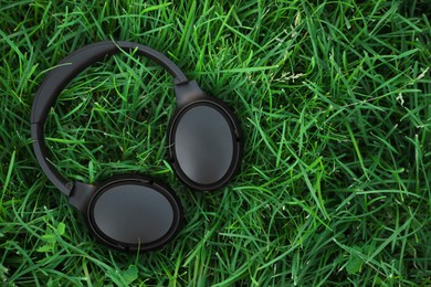 Photo of Black wireless headphones on green grass outdoors, top view. Space for text