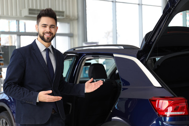 Photo of Young salesman near new car in dealership