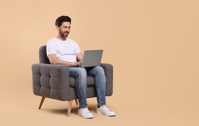 Photo of Happy man with laptop sitting in armchair against beige background. Space for text