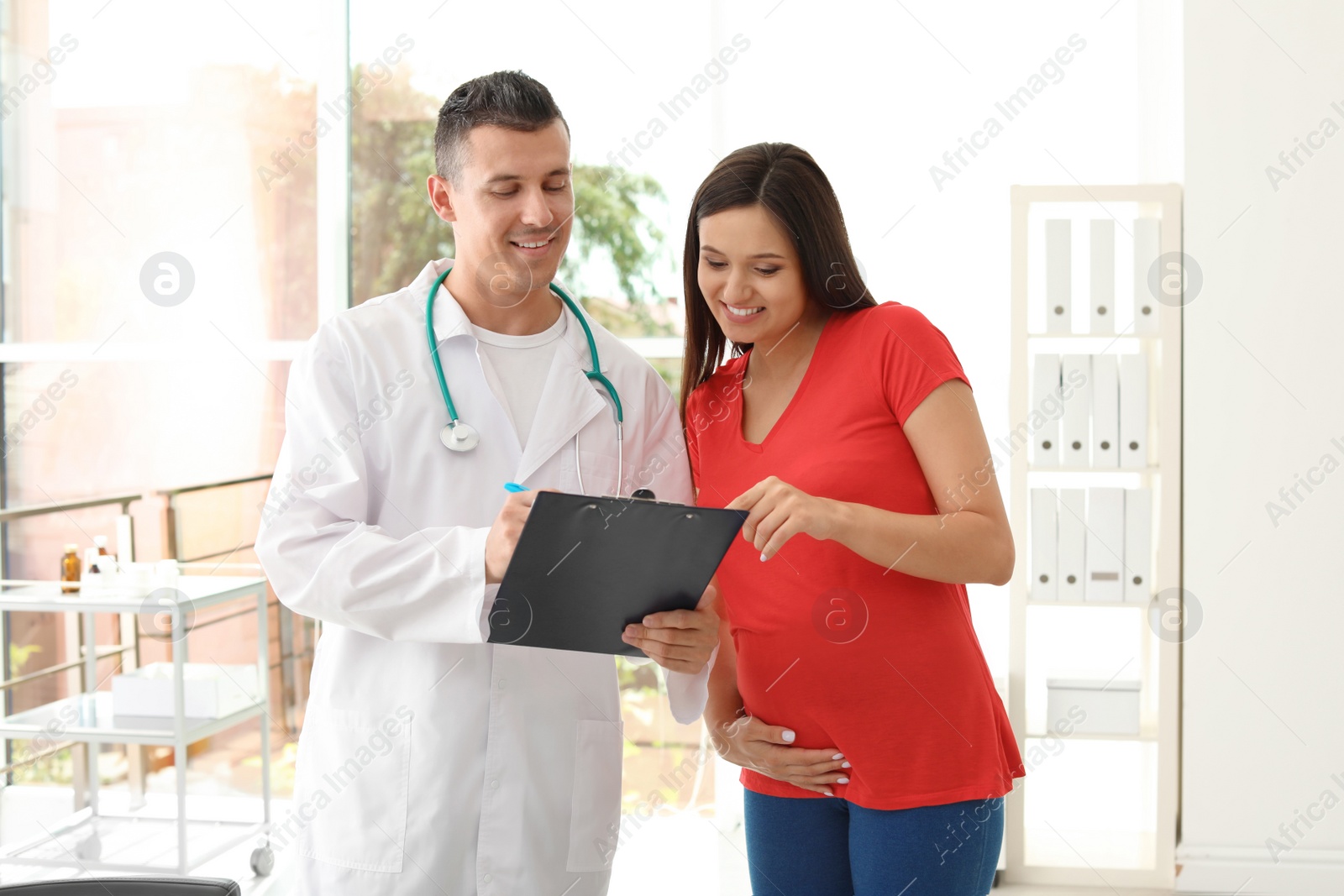 Photo of Young doctor with pregnant woman in hospital. Patient consultation