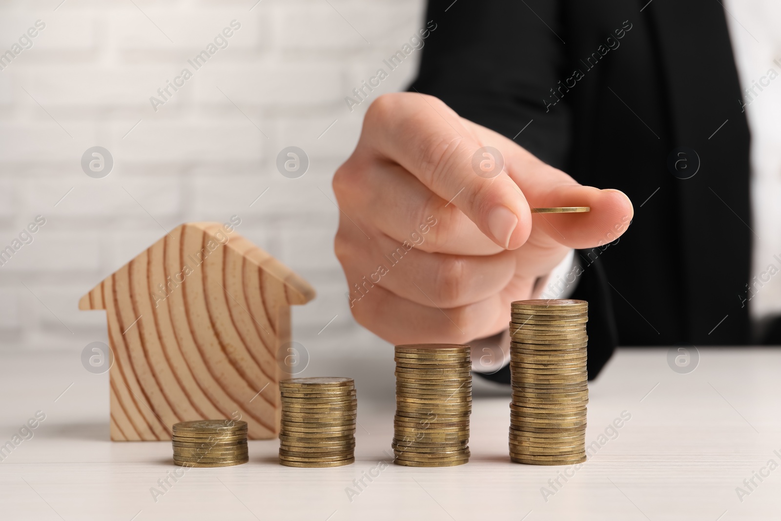 Photo of Woman stacking coins near wooden house model at light table, closeup