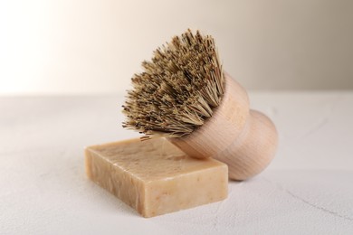 Photo of One cleaning brush and bar of soap on white textured table, closeup