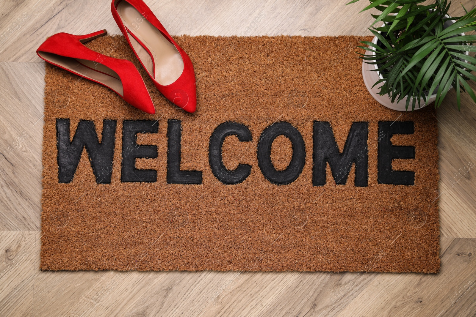 Photo of Stylish door mat with word Welcome, houseplant and shoes on wooden floor, top view