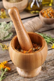 Photo of Mortar with pestle and calendula flowers on wooden table. Medicinal herbs