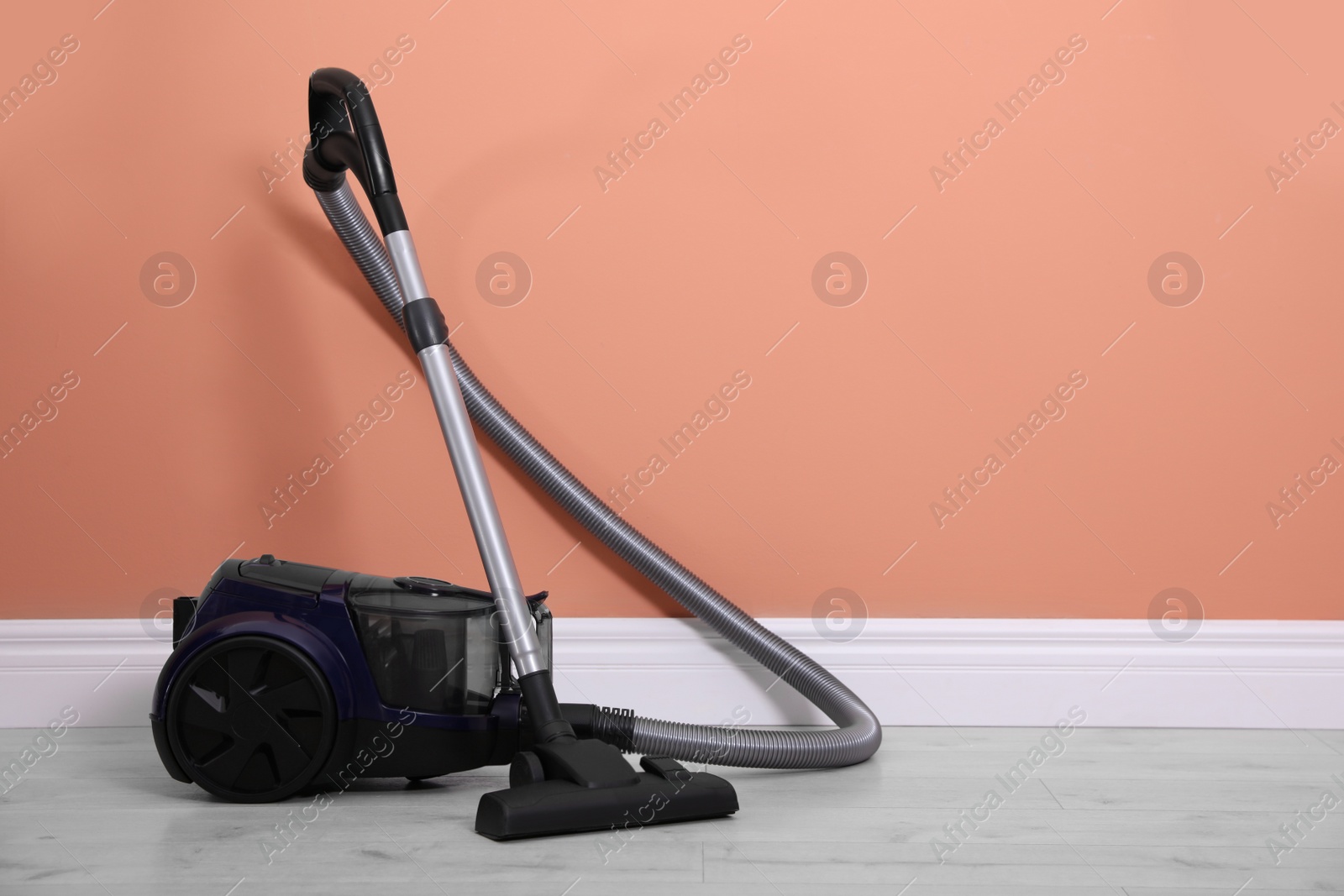 Photo of Modern vacuum cleaner on floor near orange wall indoors. Space for text