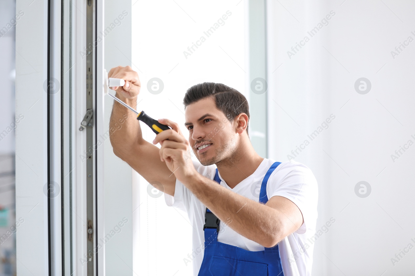 Photo of Construction worker repairing plastic window with screwdriver indoors