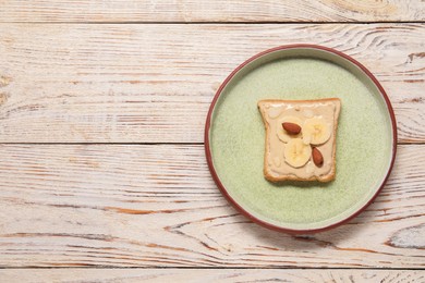 Photo of Toast with tasty nut butter, banana slices and almonds on light wooden table, top view. Space for text