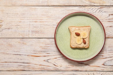 Toast with tasty nut butter, banana slices and almonds on light wooden table, top view. Space for text