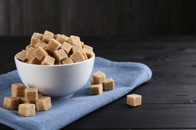 Photo of Brown sugar cubes on black wooden table, space for text