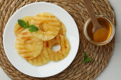 Photo of Tasty grilled pineapple slices, honey and mint on white table, top view
