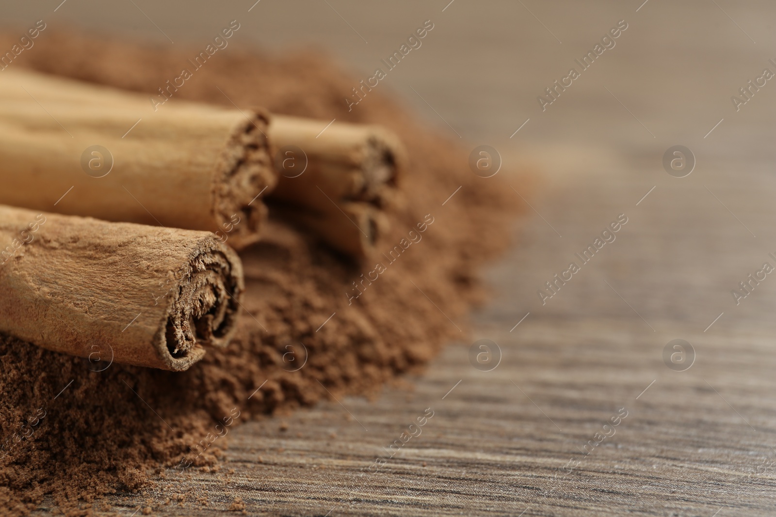 Photo of Cinnamon powder and sticks on wooden table, closeup. Space for text