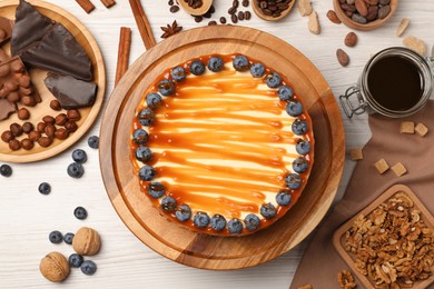 Delicious cheesecake with caramel and blueberries on white wooden table, flat lay