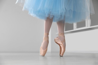 Photo of Ballerina in pointe shoes and light blue skirt dancing indoors, closeup