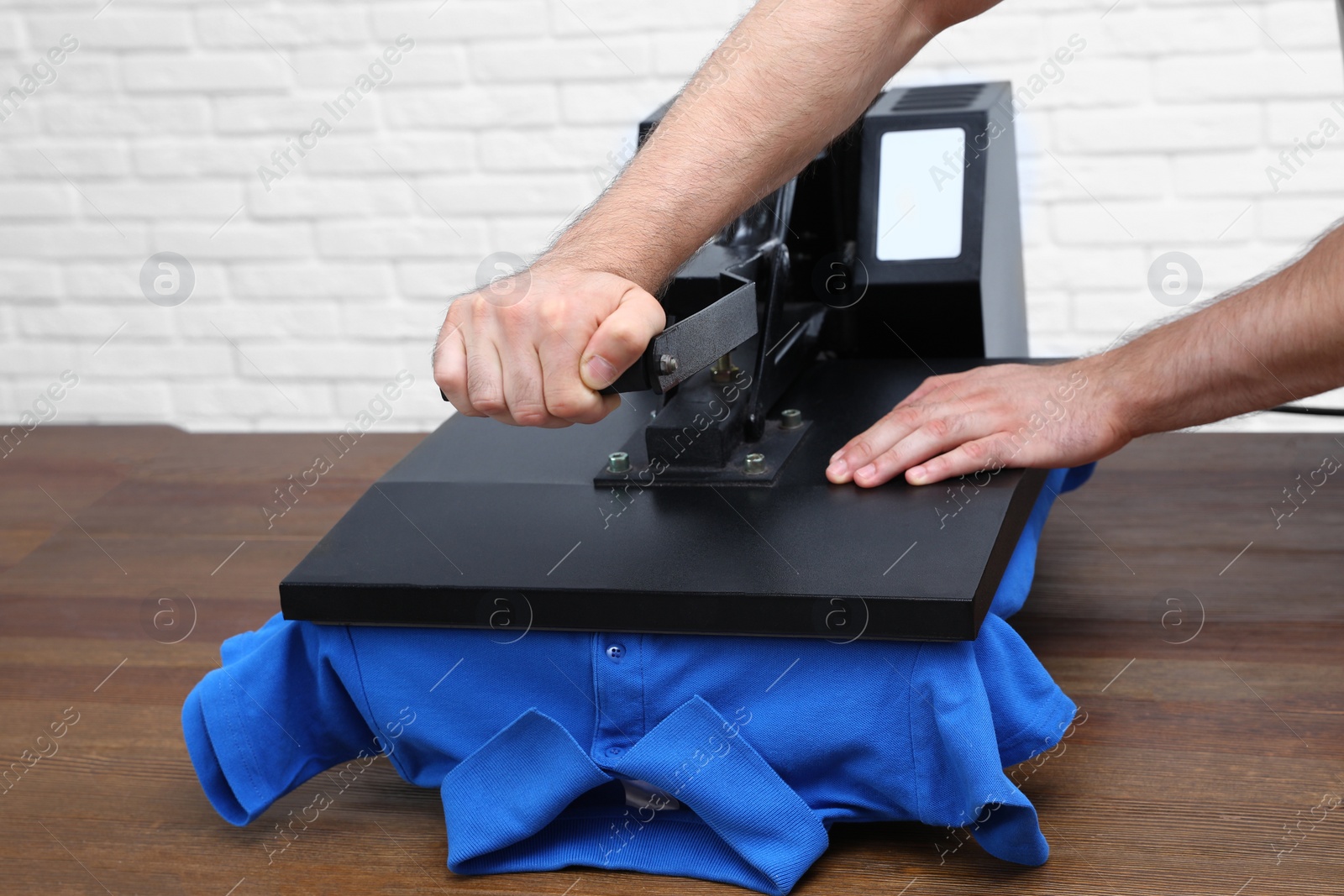 Photo of Man using heat press machine at table near white brick wall, closeup