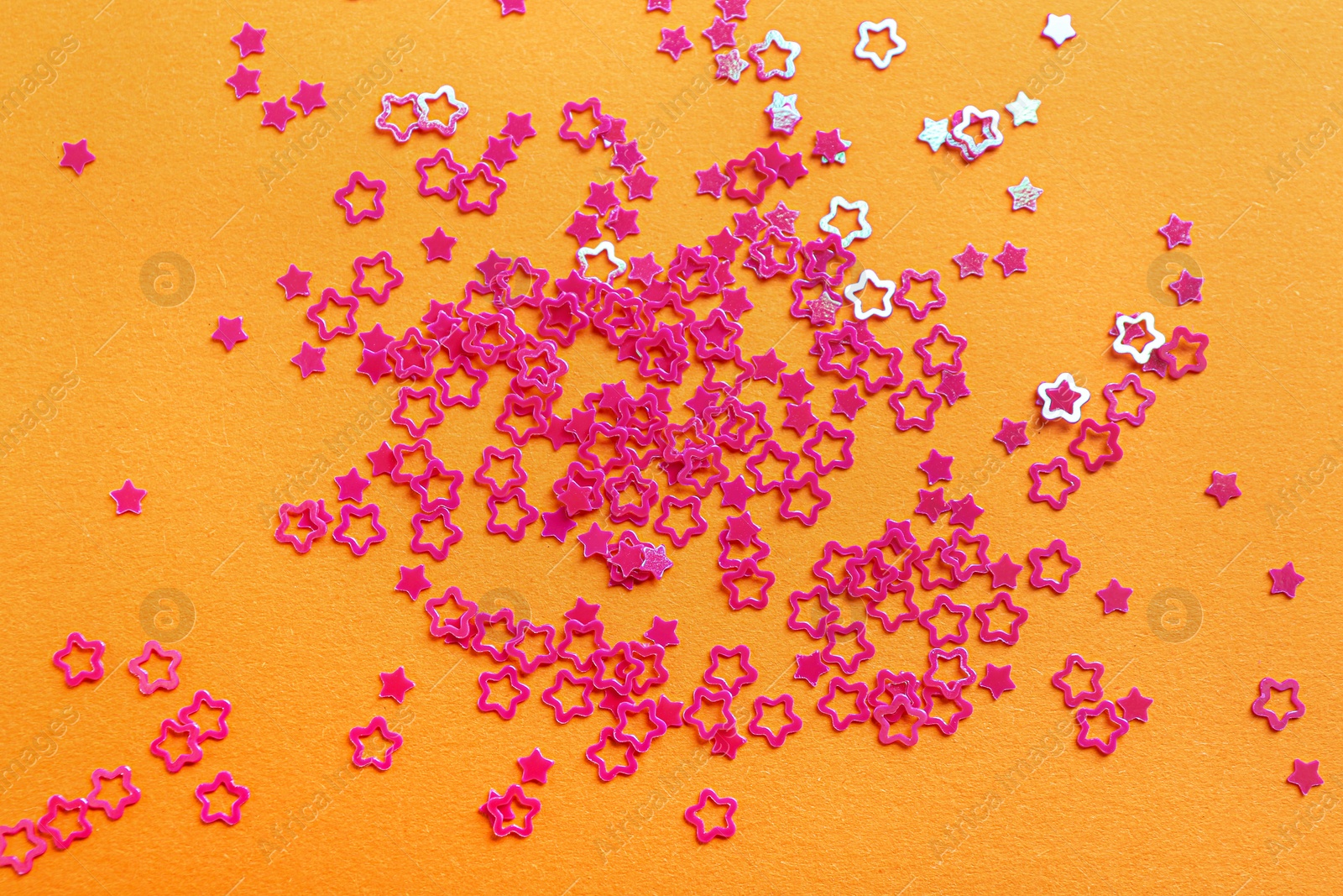 Photo of Shiny bright star shaped glitter on pale orange background