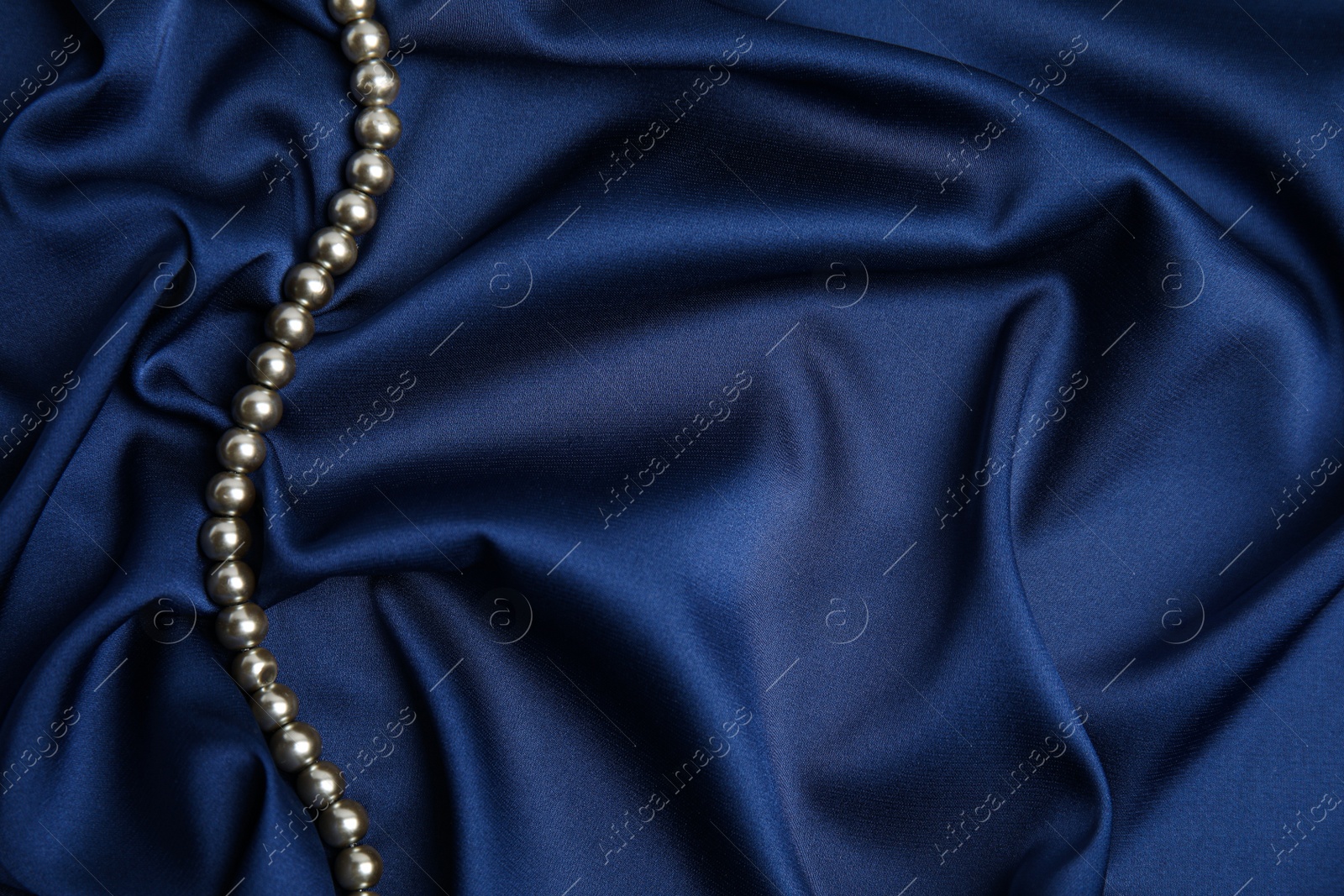 Photo of Beautiful pearls on dark blue silk, top view. Space for text