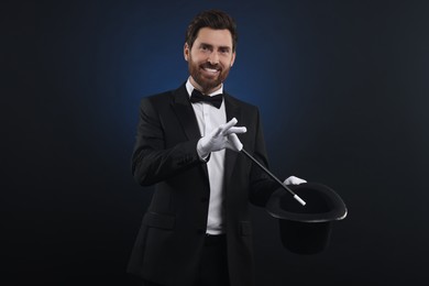 Photo of Happy magician showing magic trick with top hat on dark blue background