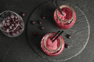 Photo of Flat lay composition with jars of delicious acai juice and cocktail straws on dark table