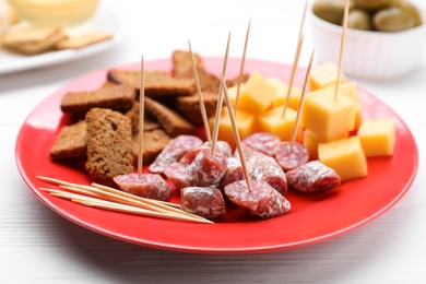 Photo of Toothpick appetizers. Pieces of sausage, cheese and croutons on white wooden table