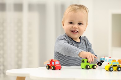 Children toys. Cute little boy playing with toy cars at white table in room, space for text