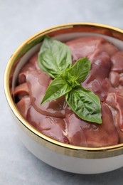 Photo of Bowl with raw chicken liver and basil on light grey table, closeup