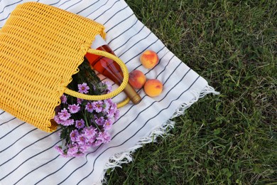 Yellow wicker bag with beautiful flowers, bottle of wine and peaches on picnic blanket outdoors