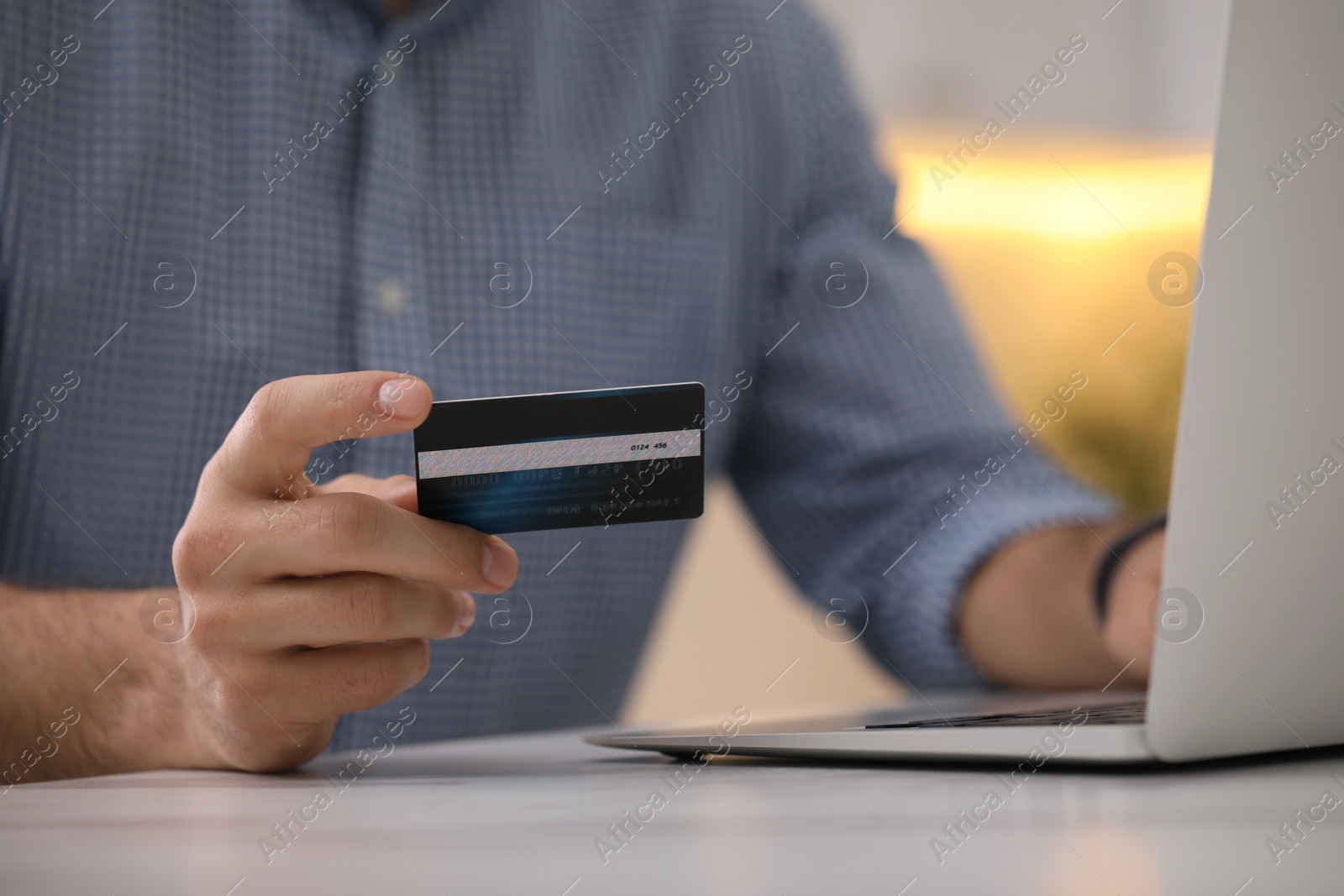 Photo of Man using laptop and credit card for online payment at table indoors, closeup