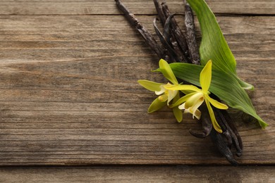 Photo of Vanilla pods, beautiful flowers and green leaves on wooden table. Space for text
