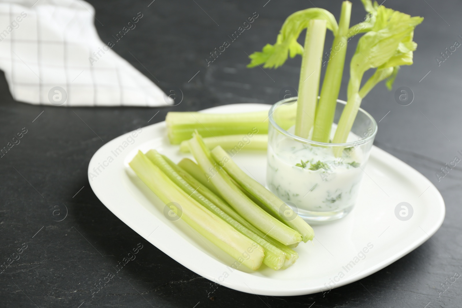 Photo of Celery sticks with dip sauce in glass on black table, closeup