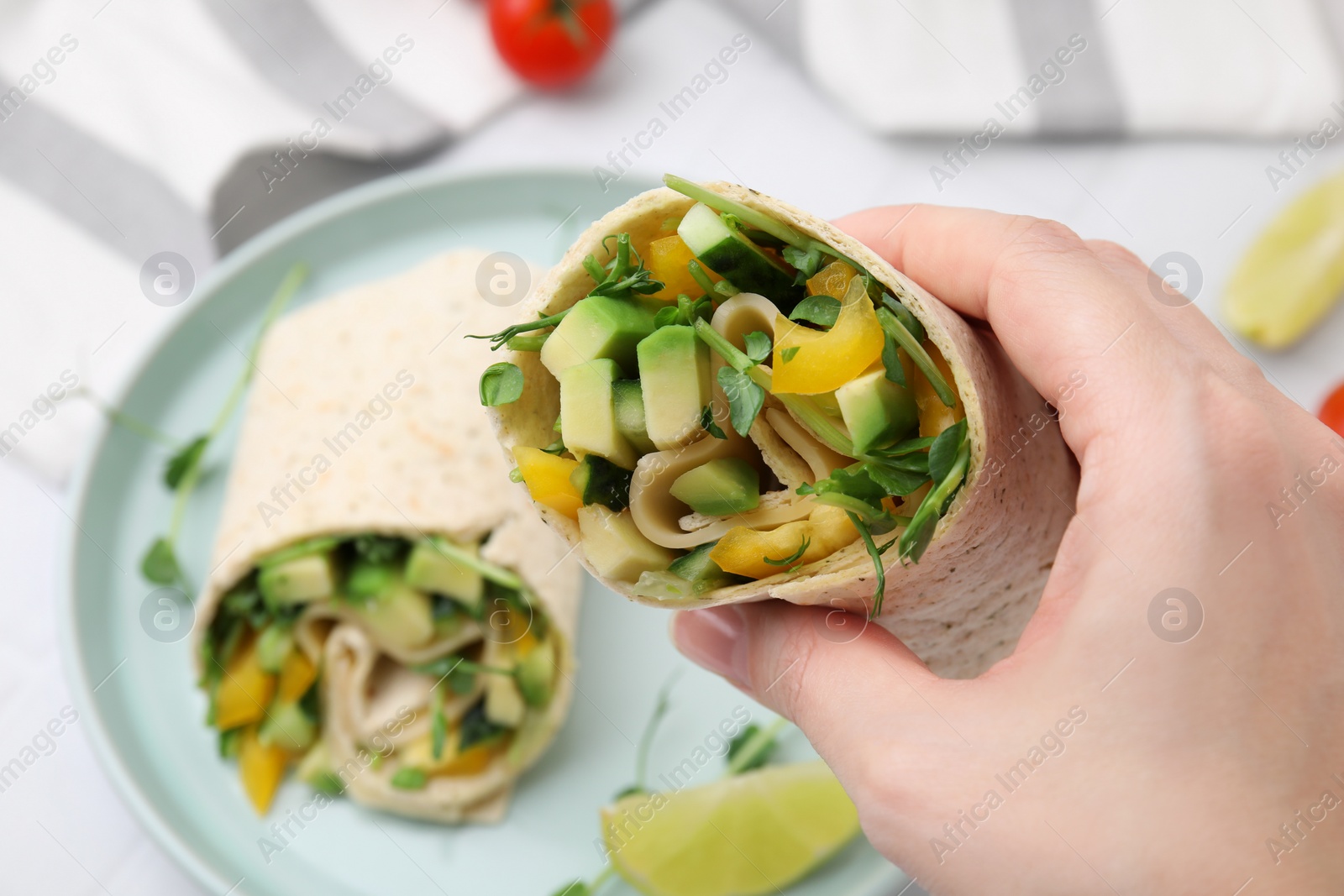 Photo of Woman holding delicious sandwich wrap with fresh vegetables at white table, closeup