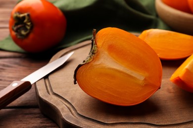 Photo of Delicious ripe persimmons and knife on wooden board, closeup