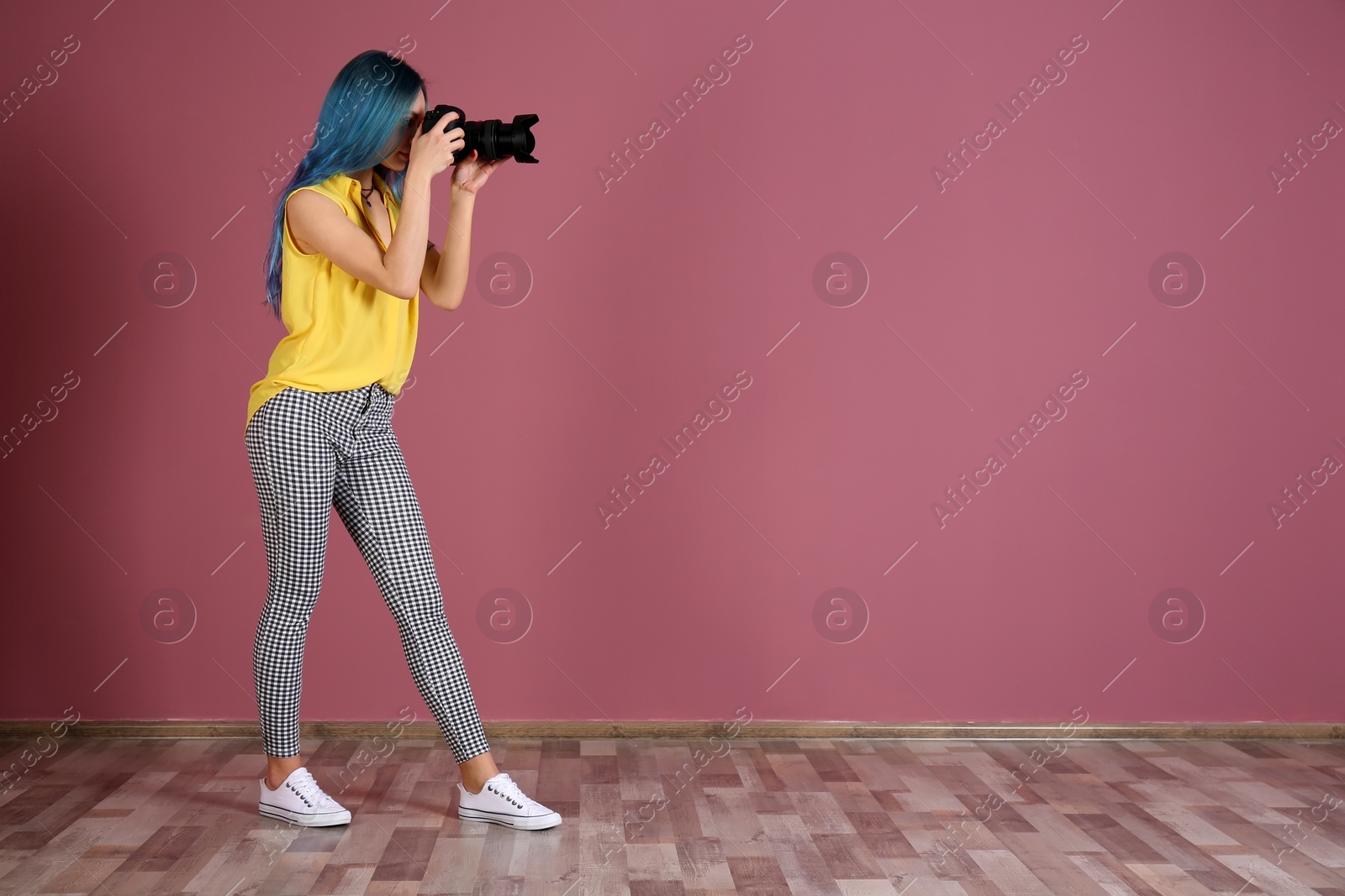 Photo of Young female photographer with camera near color wall