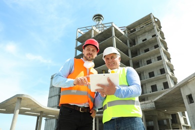 Photo of Professional engineer with tablet and foreman in safety equipment at construction site