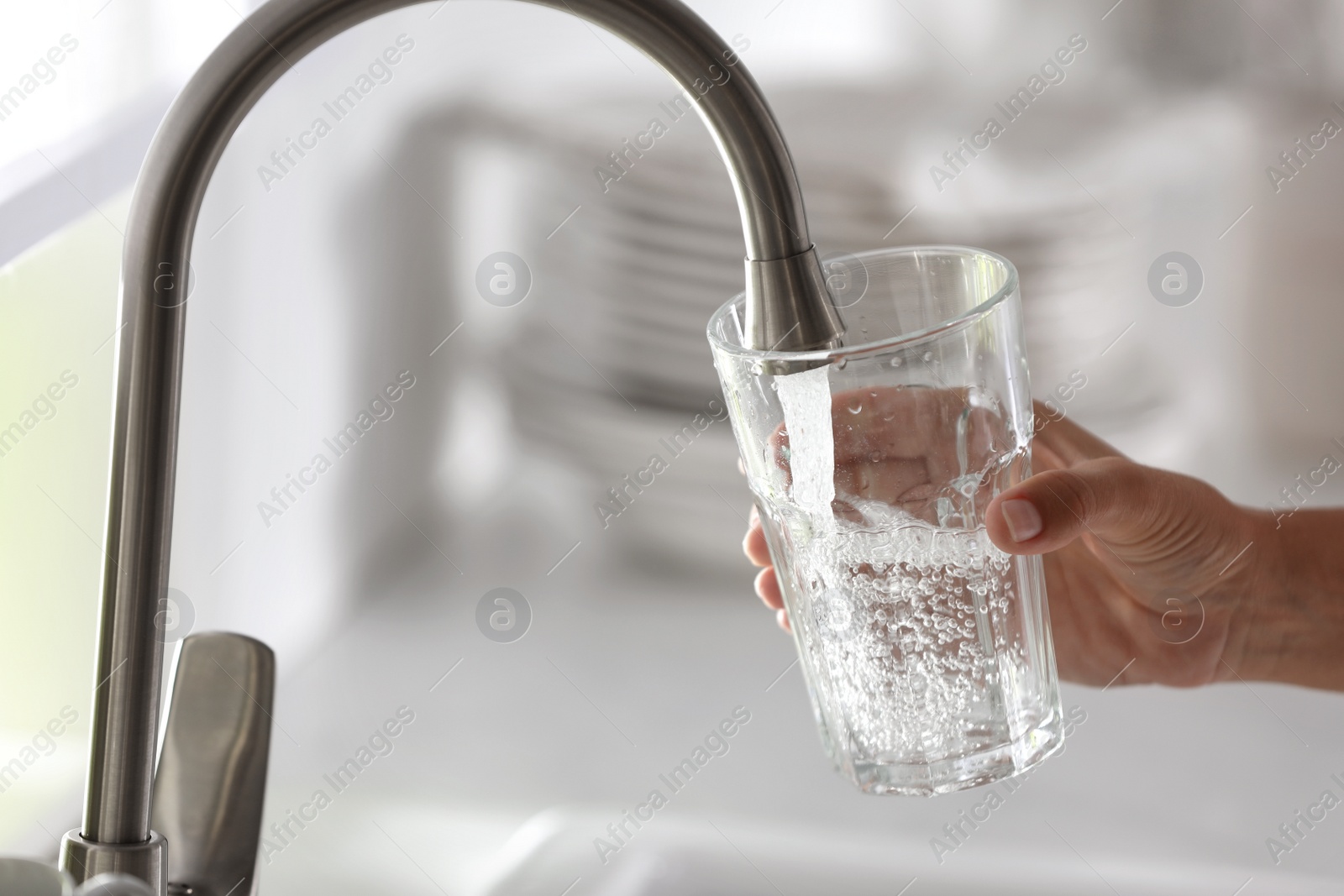 Photo of Woman pouring water into glass in kitchen, closeup