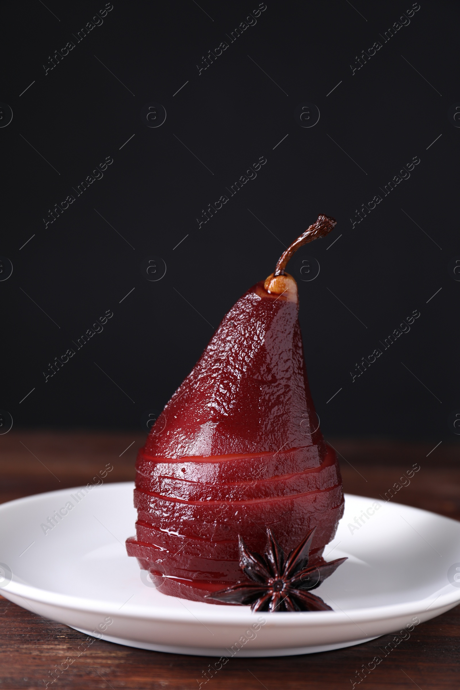 Photo of Tasty red wine poached pear and anise on wooden table, closeup