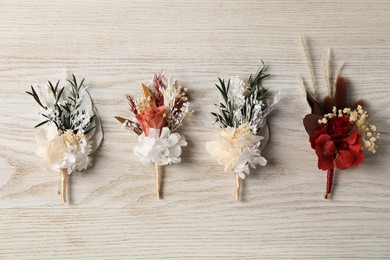 Stylish boutonnieres on white wooden table, flat lay