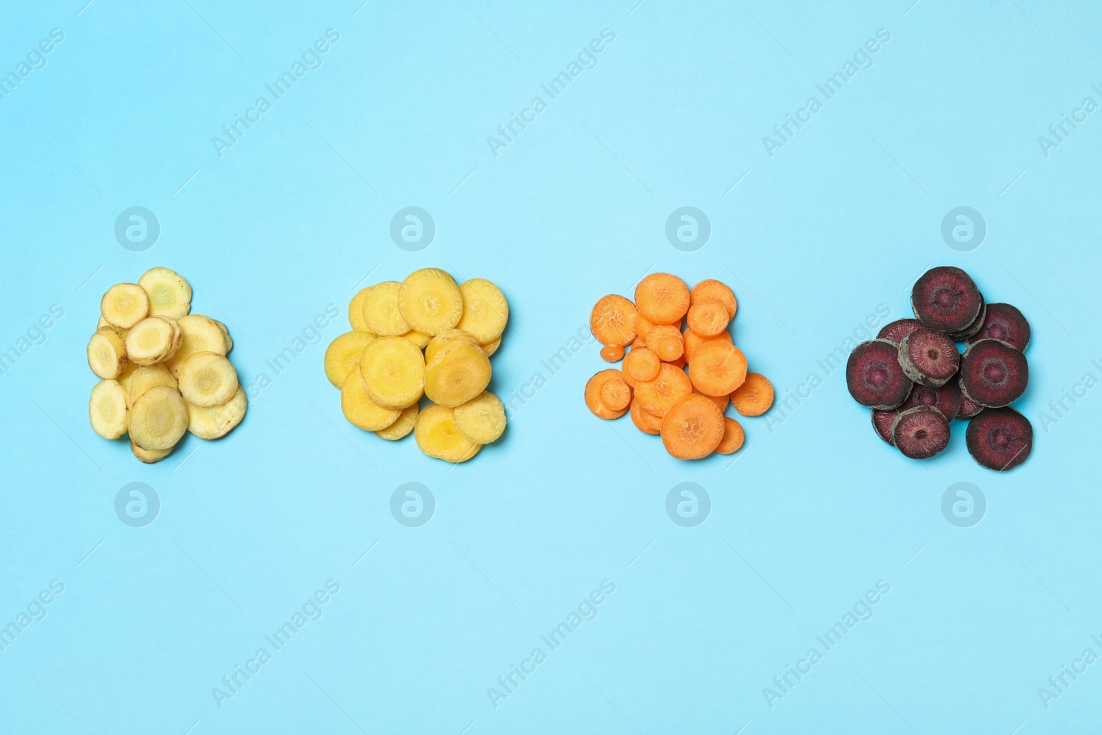 Photo of Slices of raw color carrots on light blue background, flat lay