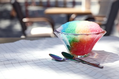 Photo of Rainbow shaving ice in glass dessert bowl and spoons on table outdoors