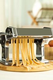 Pasta maker with raw dough on white table, closeup